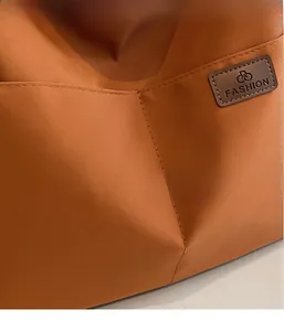 Detail of orange-brown canvas fabric and stitched leather logo patch on shoulder bag