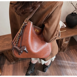 Detail of a brown leather bucket bag with braided tassels and small dog charm