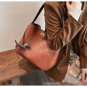 Close-up of caramel leather tote bag featuring a metal twist lock and a cute dog pendant