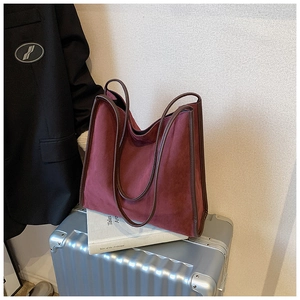 Detailansicht einer burgunderroten Wildleder-Tote-Bag mit braunem Rand auf einem Koffer