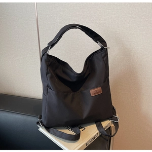 Detail of black nylon shoulder bag showing front pocket and brown leather logo patch