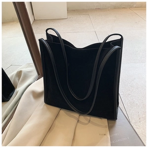 Minimalistische schwarze Wildleder-Einkaufstasche mit langen Riemen neben einem Trenchcoat
