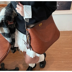 Detail of caramel leather bucket bag with dog-shaped charm and gold metal clasp closure