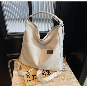 Detail of cream-colored canvas tote bag featuring a leather fashion logo and silver rings