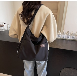 Detail of adjustable strap and side pocket on black nylon crossbody bag worn by model