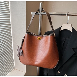 Detailed close-up of brown PU leather tote with brass twist lock and cat-shaped charm