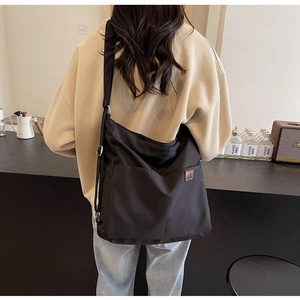 Detail of the black canvas tote bag showing the side leather logo and adjustable strap