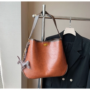 Detail of a large brown faux leather tote bag with gold turn-lock and horse charm decoration