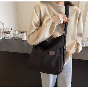 Detailed view of black canvas crossbody bag with adjustable strap and leather logo tag