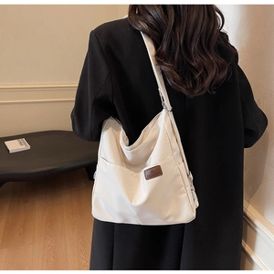 Close-up of white canvas tote bag with brown leather label and wide shoulder strap
