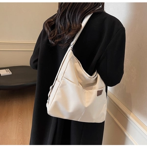 Detail view of cream-white hobo shoulder bag with fashion leather tag on minimalist coat