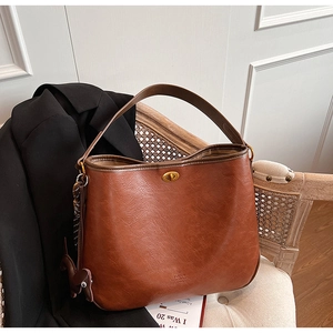 Detail einer braunen Eimer-Tasche mit Drehverschluss und Anhänger auf einem Webstuhl
