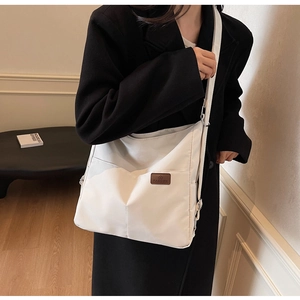 Detail of a white canvas crossbody bag with a brown heart logo worn by a model