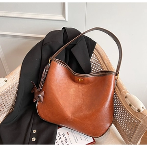 Detail der braunen Ledertasche mit goldenem Drehverschluss und Anhänger auf Vintage-Stuhl
