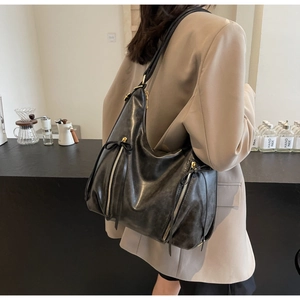 Detail showing the large black PU leather tote bag worn by a model in a beige suit