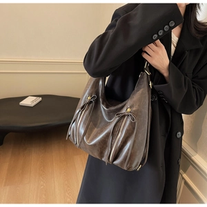 Detail of dark brown leather tote bag featuring metal zippers and bow drawstring accent