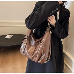 Detail of vintage brown leather hobo bag with decorative zippers and tassel bow accents