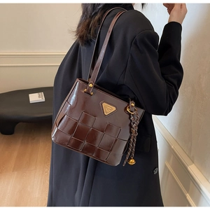 Detalle de bolso tote trenzado marrón oscuro con logo metálico triangular y borla lateral