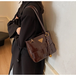Detalle de bolso tote trenzado marrón oscuro con emblema dorado y borla decorativa