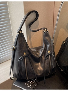 Retro black leather tote bag with vertical zippers and bow tassels in soft natural light