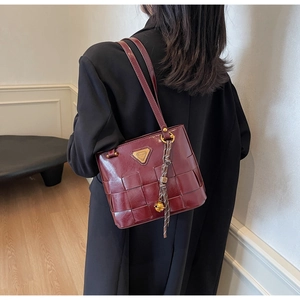 Detalle de bolso tote de cuero trenzado burdeos con emblema triangular dorado y colgante