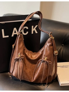 Large dark brown vintage leather shoulder bag with decorative bow zippers on a sofa