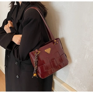 Detalle de bolso de cuero sintético burdeos con tejido ancho y placa metálica triangular