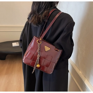 Detalle del bolso tote de cuero trenzado burdeos con logo dorado y borla en una modelo
