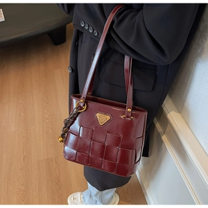 Detalle del bolso burdeos de cuero brillante con textura trenzada y logo de triángulo dorado