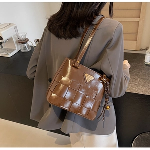 Detalle de bolso tote marrón brillante con textura trenzada y logo triangular en la correa