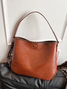 Retro brown leather tote bag with gold twist lock and woven charm in a lifestyle setting