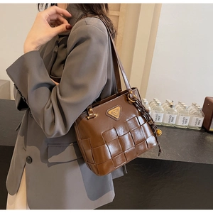 Detalle de bolso tote de cuero trenzado marrón con logo dorado sobre blazer gris