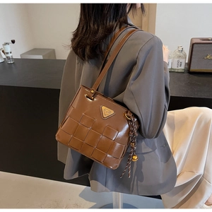 Detalle de bolso tote de cuero trenzado marrón oscuro con borla dorada y placa de metal