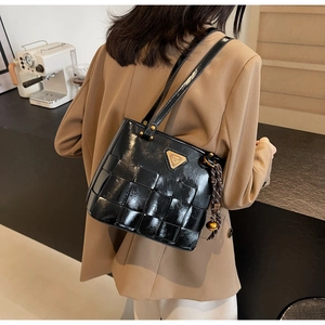 Detalle del bolso tote trenzado negro brillante con logotipo metálico y colgante