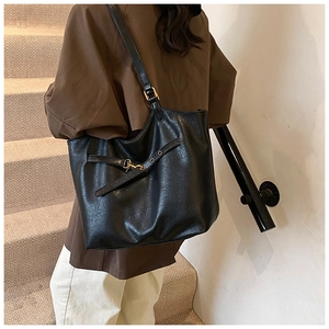 Detail of a large black leather tote bag with gold buckle strap worn by a model