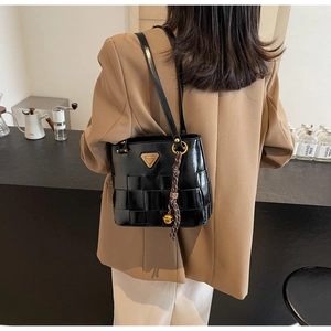 Detalle de bolso de hombro trenzado negro con logo metálico dorado y colgante de campana