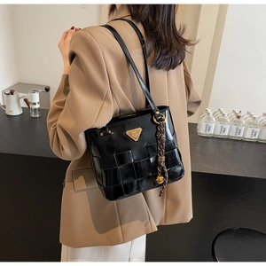 Detalle de bolso tote de cuero PU tejido negro con logotipo metálico usado por modelo