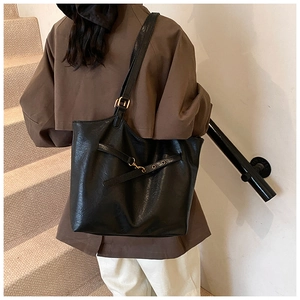 Detail view of large black tote bag with gold buckle on a model in a stairwell