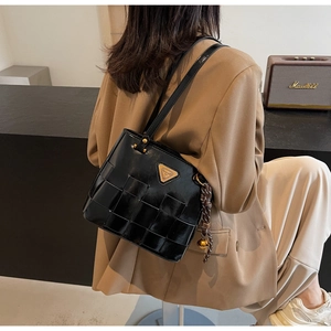 Detalle de bolso tote trenzado negro con placa dorada y colgante de campana en hombro