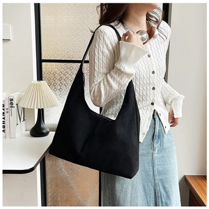 Detail view of a minimalist black hobo tote bag with a wide shoulder strap on a model