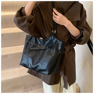 Detail of black tote bag with glossy leather texture and adjustable metal buckle strap