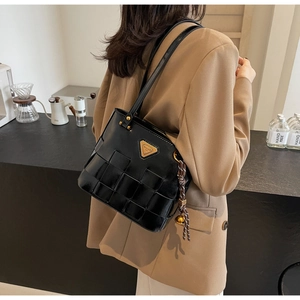 Detalle de bolso tote negro brillante trenzado con logo metálico y nudo decorativo