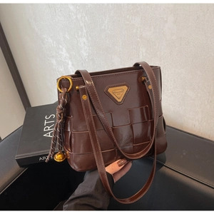 Detalle de bolso tote marrón oscuro en cuero encerado trenzado con logo metálico triangular