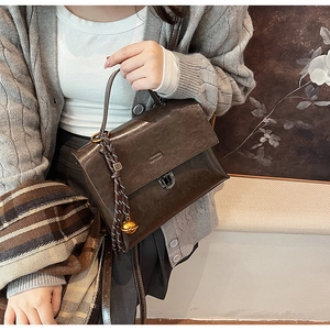 Détail du sac à main vintage en cuir marron avec breloque cloche dorée et sangle tressée