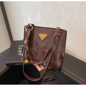 Primer plano de un bolso tote trenzado marrón oscuro con acabado brillante y logo dorado
