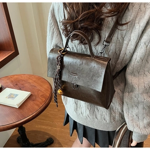 Detail der braunen Ledertasche mit geflochtener Kordel und goldenem Glockenanhänger