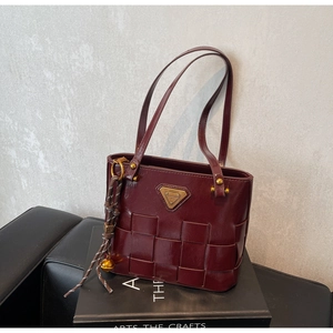 Detalle del bolso tote de cuero burdeos con textura tejida y logotipo de metal dorado