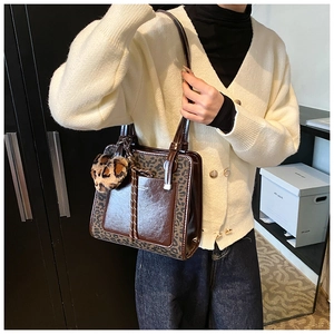 Detail of a brown leather tote with leopard print accents and heart-shaped plush charm