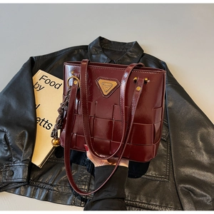 Primer plano de bolso tote trenzado rojo oscuro con logo triangular dorado sobre chaqueta
