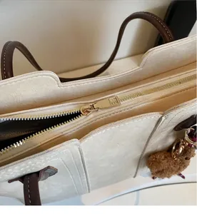 Close-up of smooth gold metal zipper closure on the off-white tote bag detail